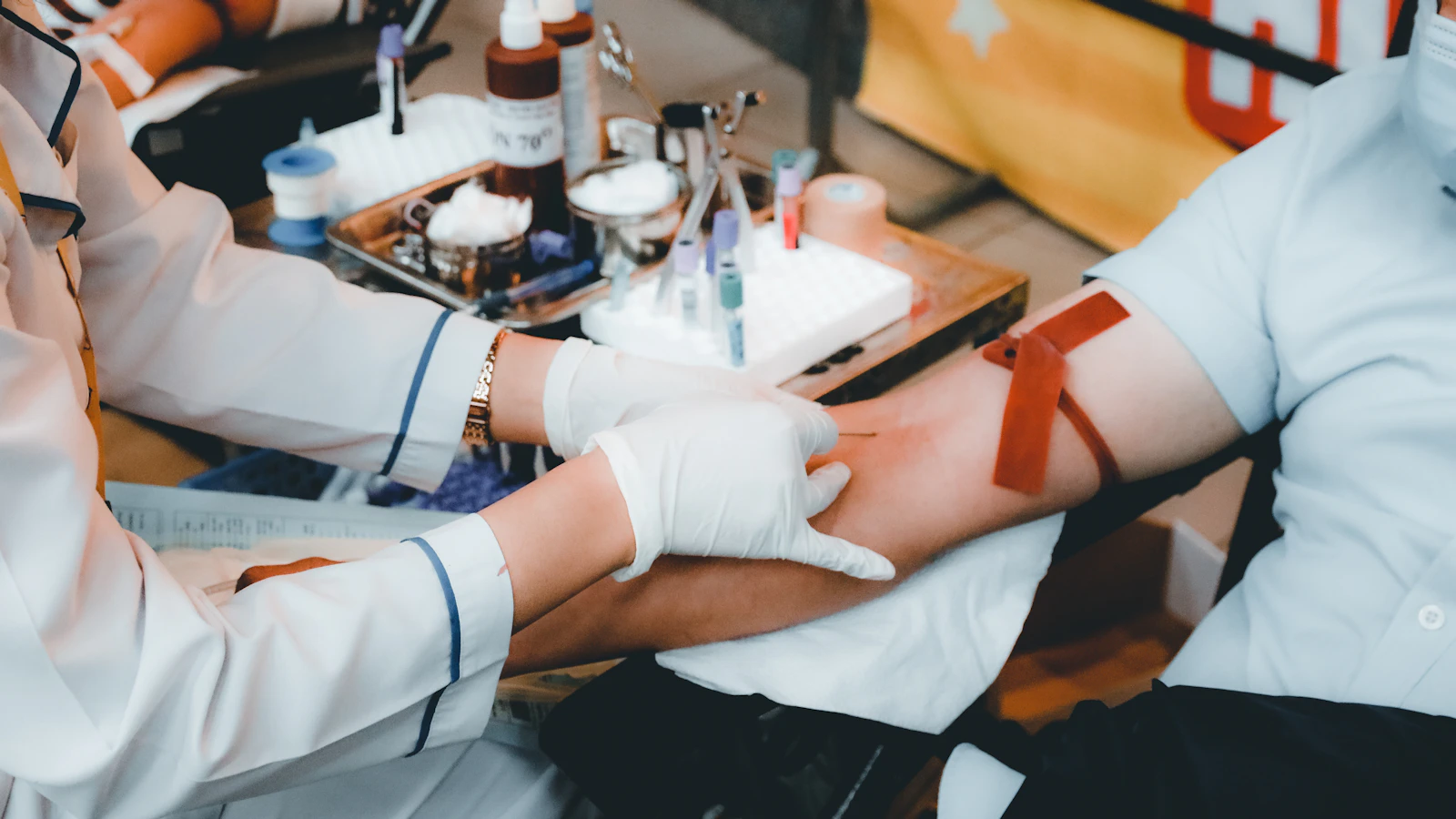 A professional draws blood from the arm with a tourniquet at a collection point.