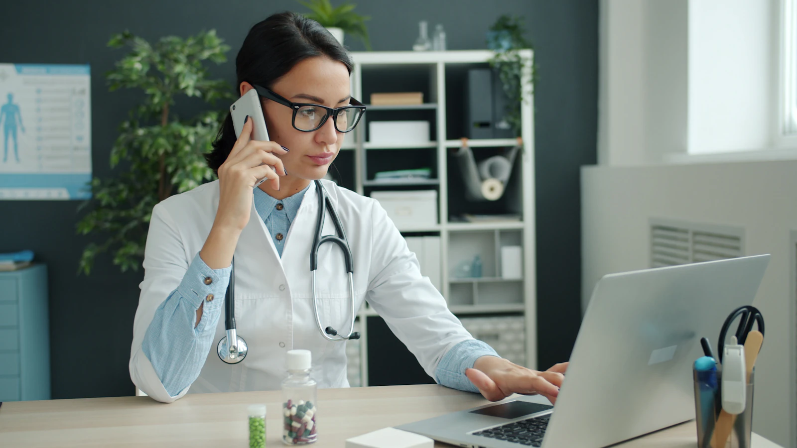 A doctor reviews medical results at a computer with a stethoscope on the desk.