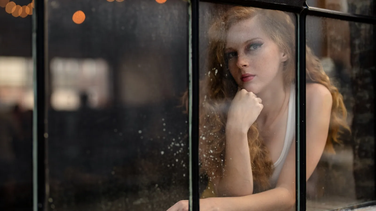 Volwassen vrouw kijkt bedachtzaam uit het raam, als beeld bij coeliakie symptomen bij volwassenen.