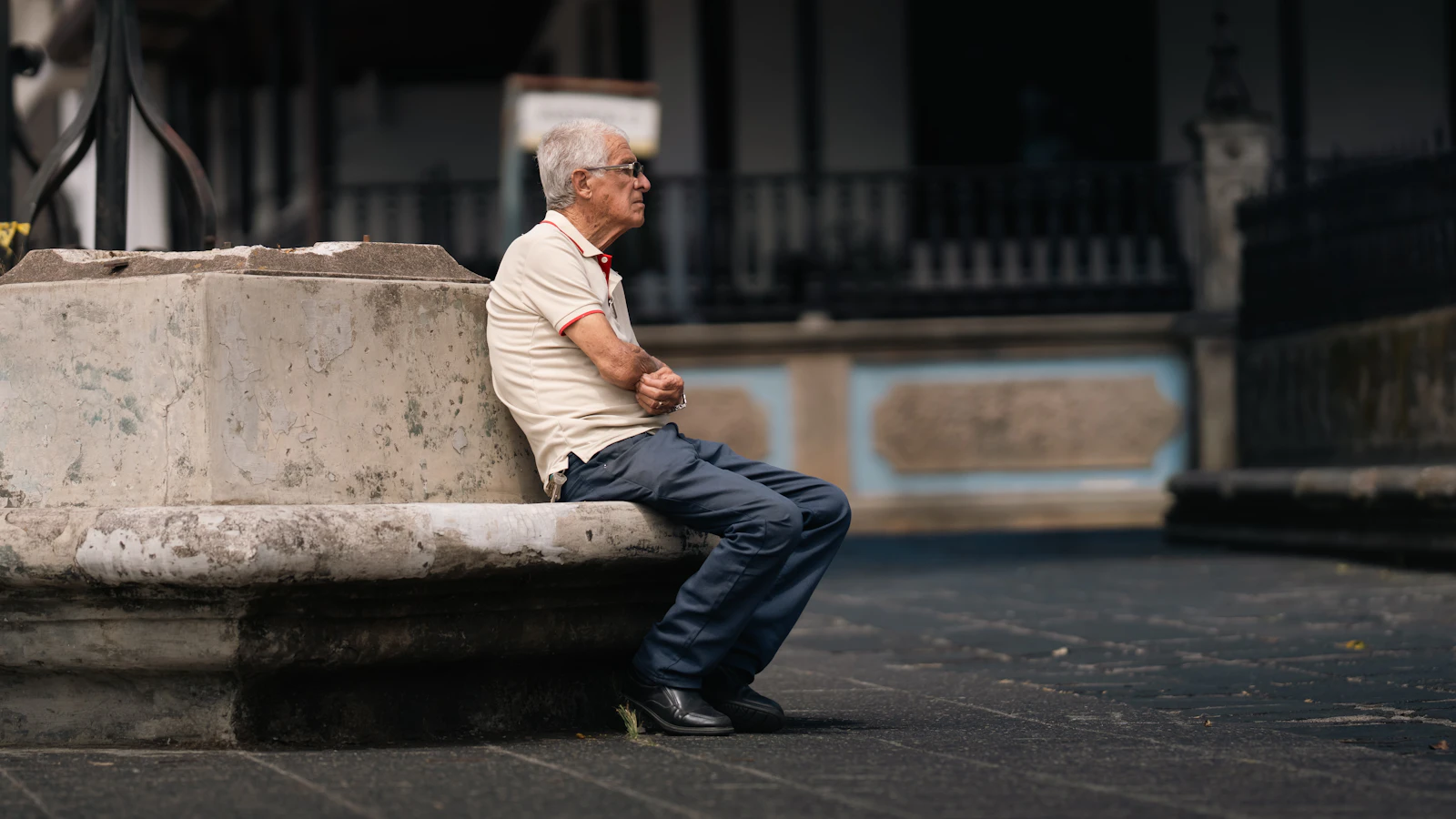 An older man sits relaxed on a bench outdoors.