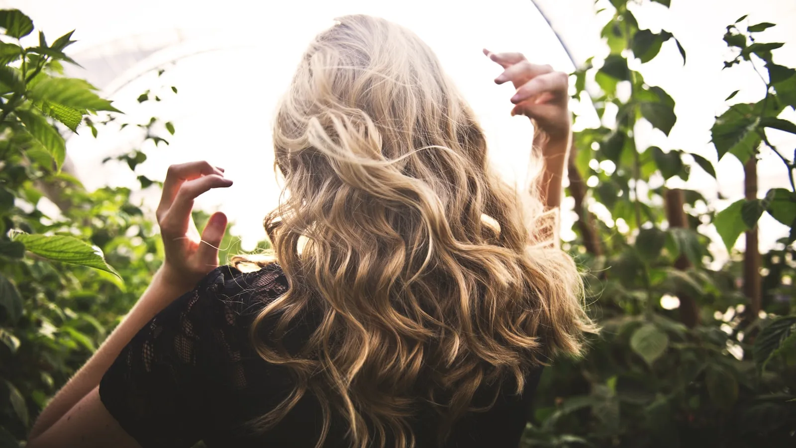 Een blonde vrouw tussen hoge groene planten in daglicht.