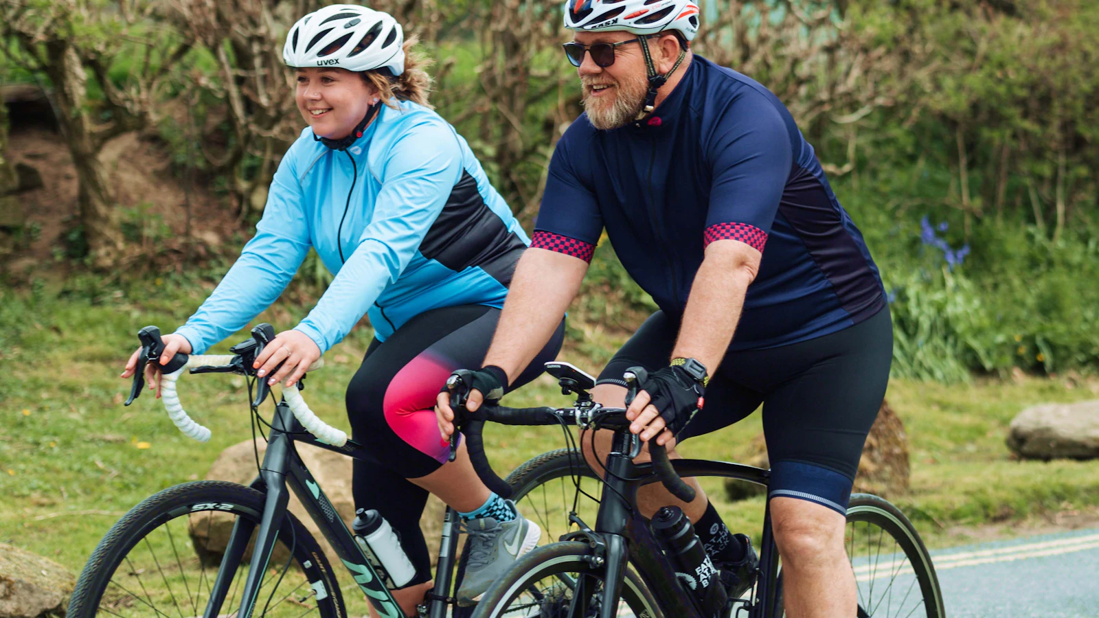 Een man en vrouw fietsen samen in sportkleding buiten op een landweg.