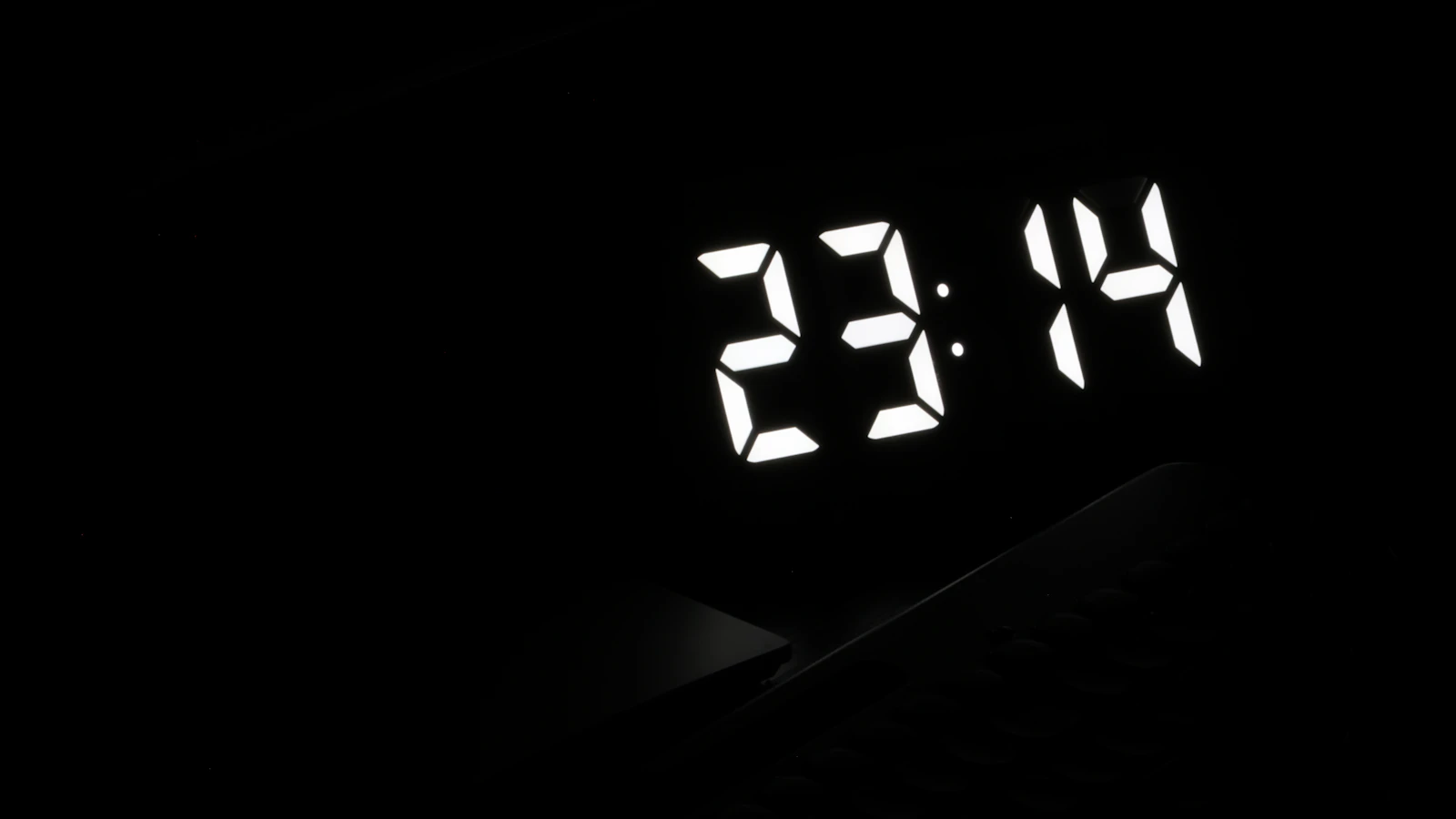 Digital alarm clock showing 23:14 in a dark bedroom