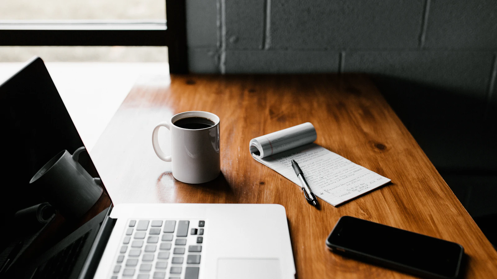 Kop koffie naast een laptop op een houten bureau