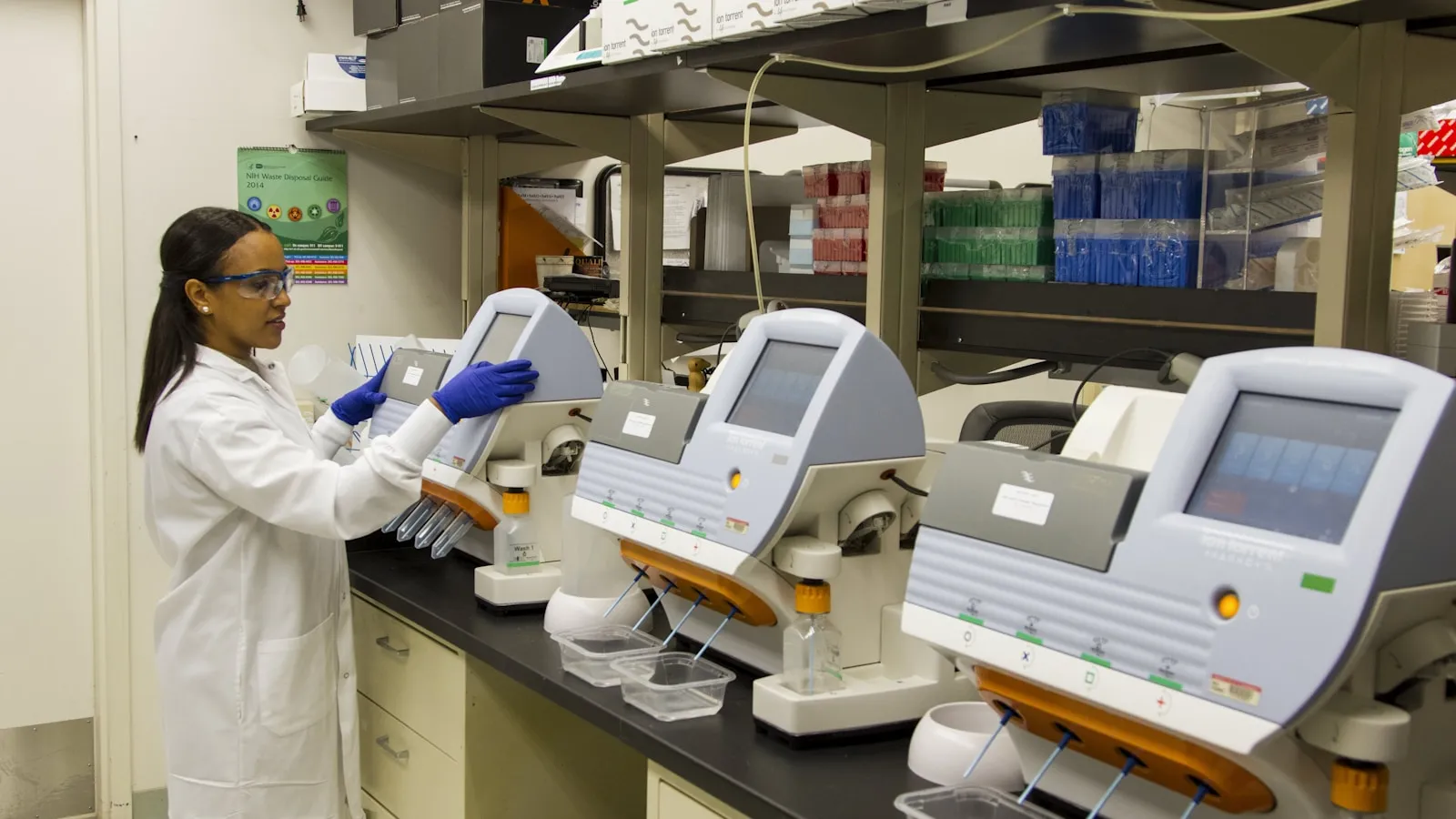 Een laborante werkt aan een rij analyseapparaten in een laboratorium.