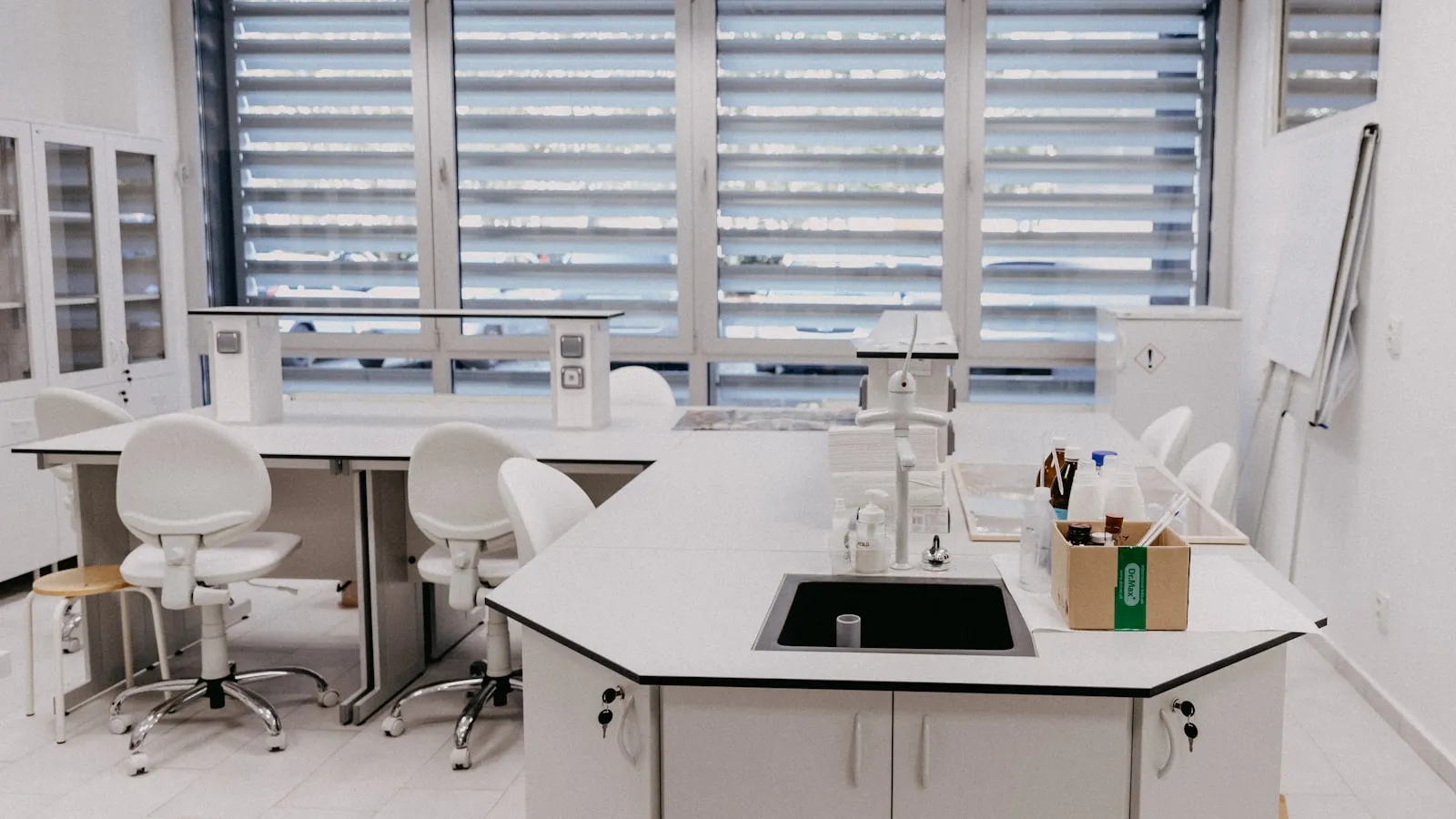 Een opgeruimde laboratoriumruimte met een witte werkbank en krukken bij het raam.