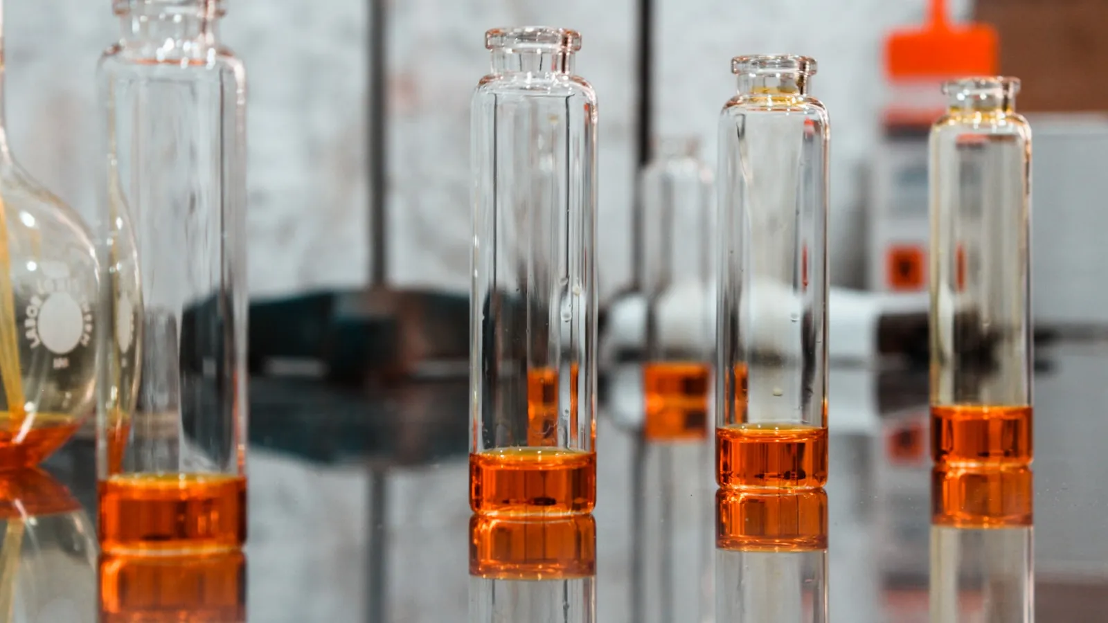 Glazen laboratoriumflesjes met een oranje vloeistof op een werkbank.