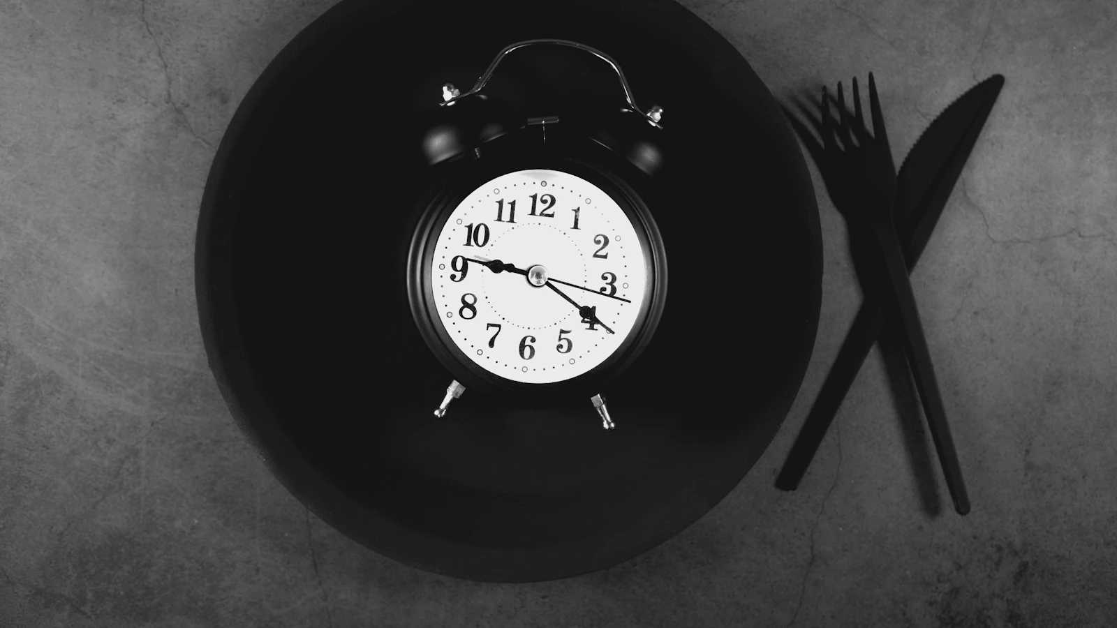 Een bord met bestek naast een klok, als beeld bij intermittent fasting en je bloedwaarden.