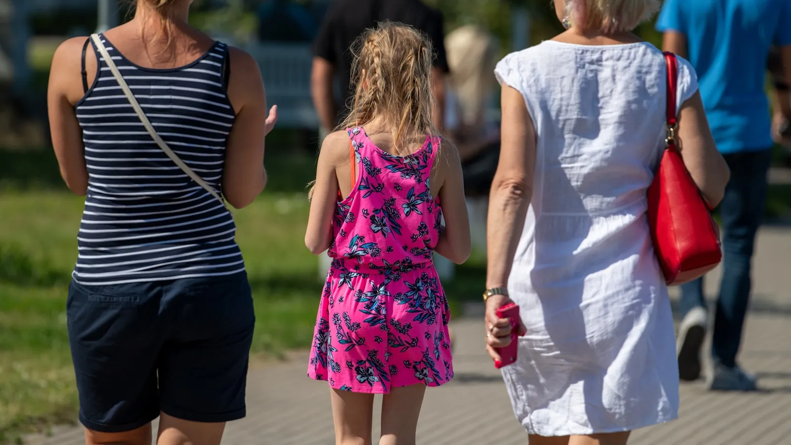 Twee vrouwen en een meisje wandelen samen door een park.