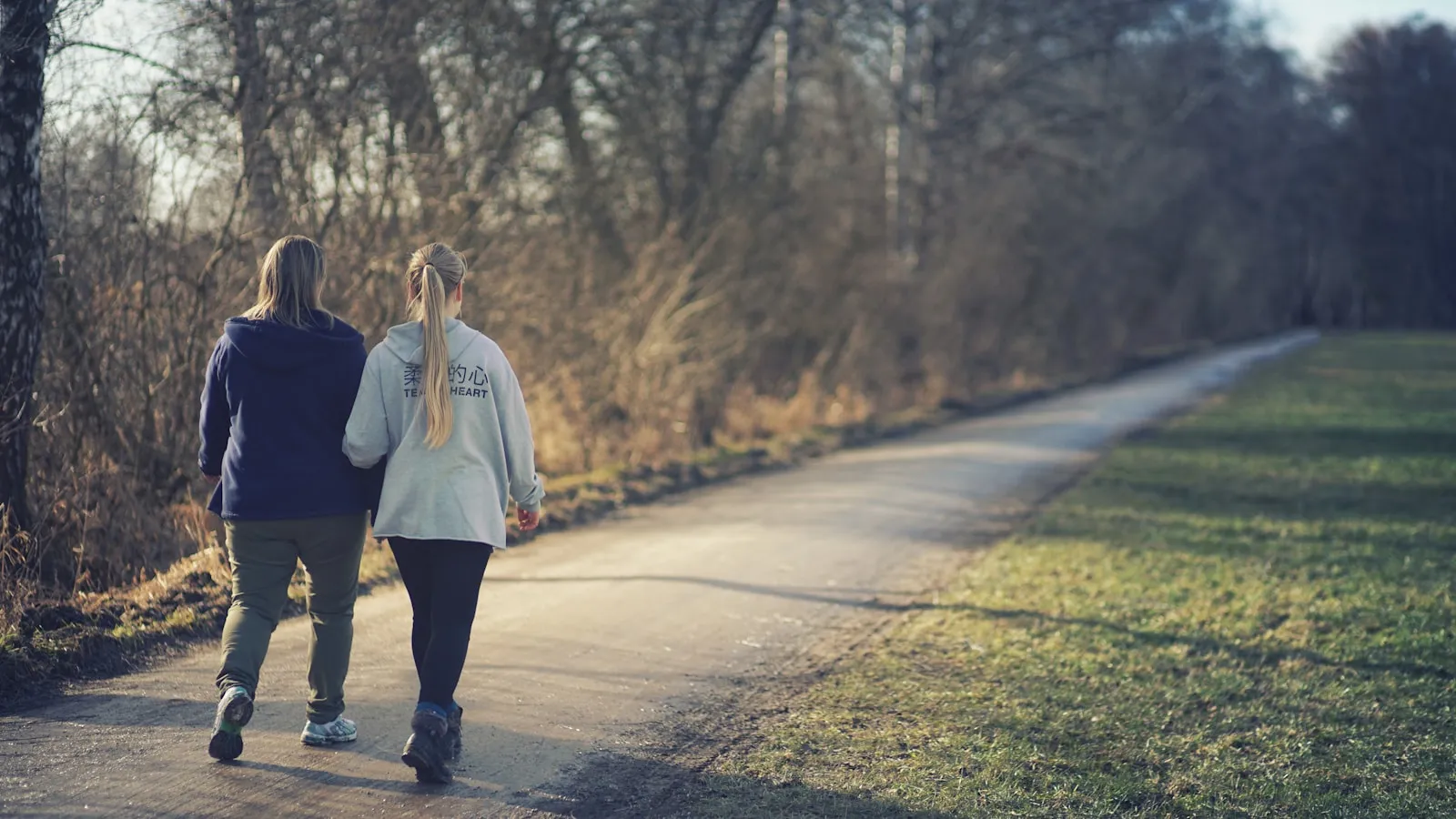 Twee mensen wandelen samen over een pad langs een grasveld in het najaar.