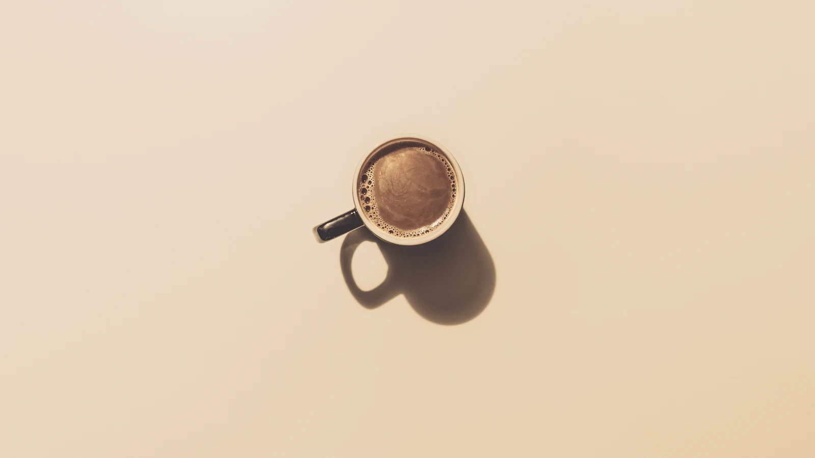 Een dampende kop zwarte koffie naast een bloedbuisje op een lichte tafel, als beeld bij koffie en bloedwaarden.