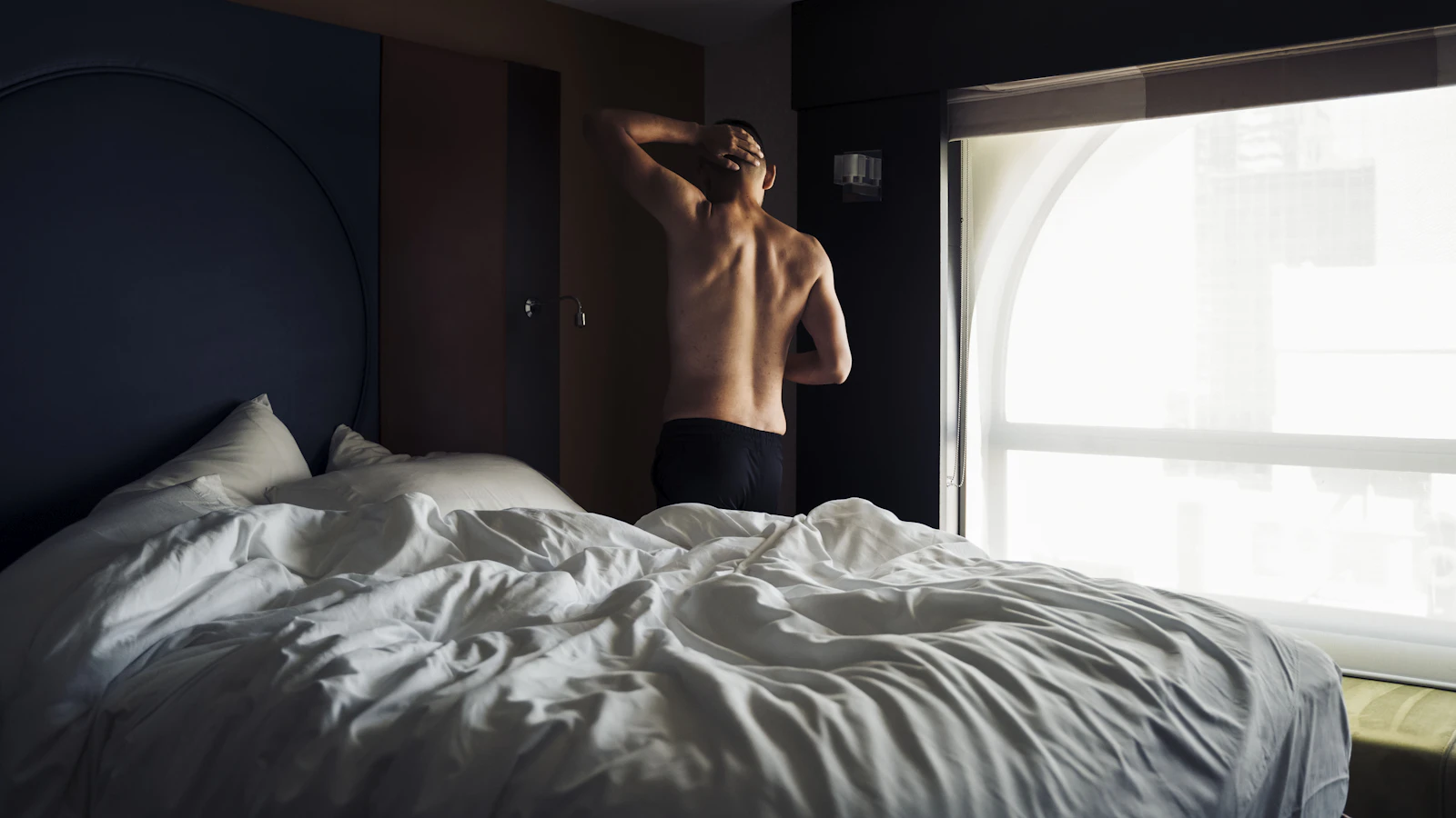 Iemand zit moe op de rand van het bed in de ochtend, als beeld bij moe zijn ondanks genoeg slaap.