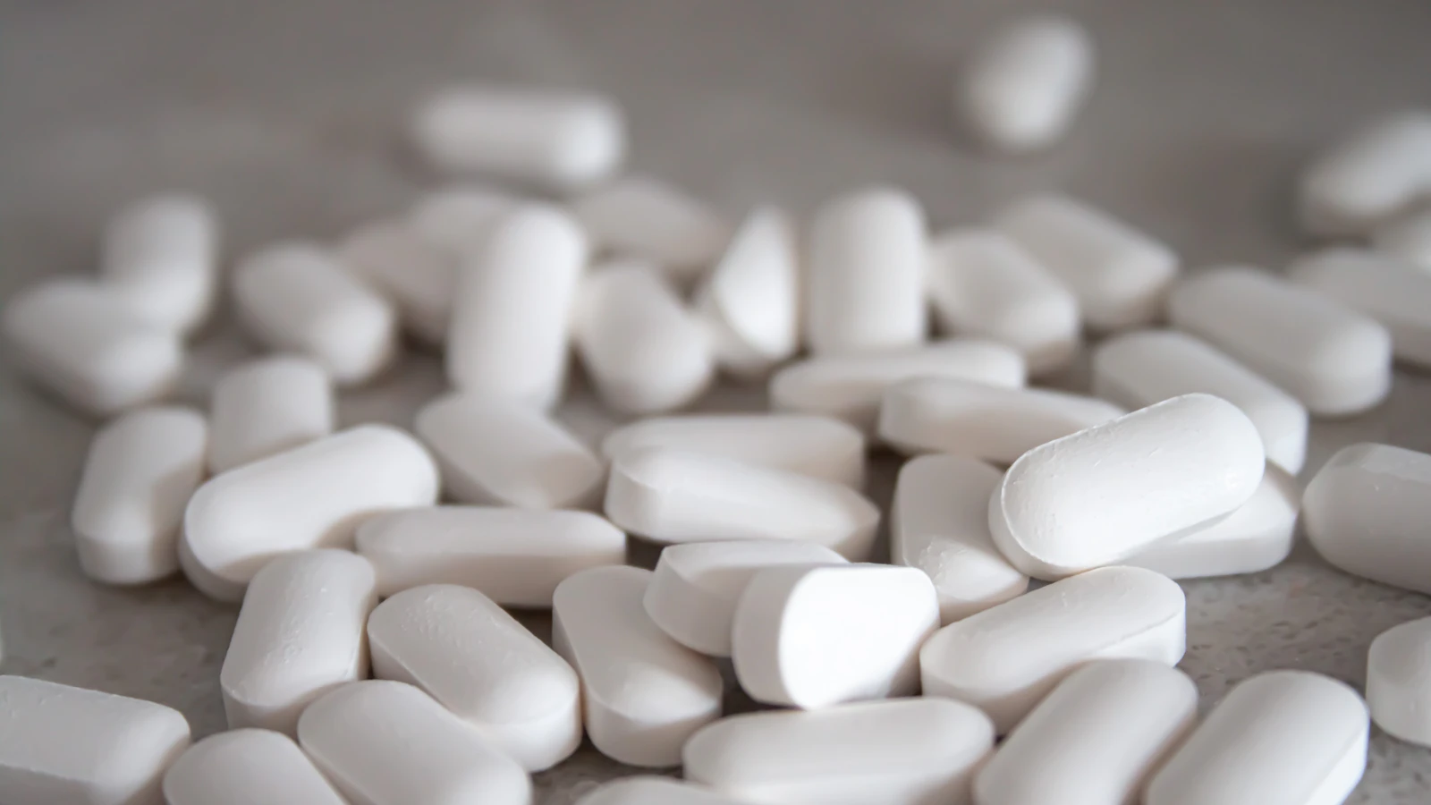 Witte ovale tabletten liggen verspreid op een bruin oppervlak.