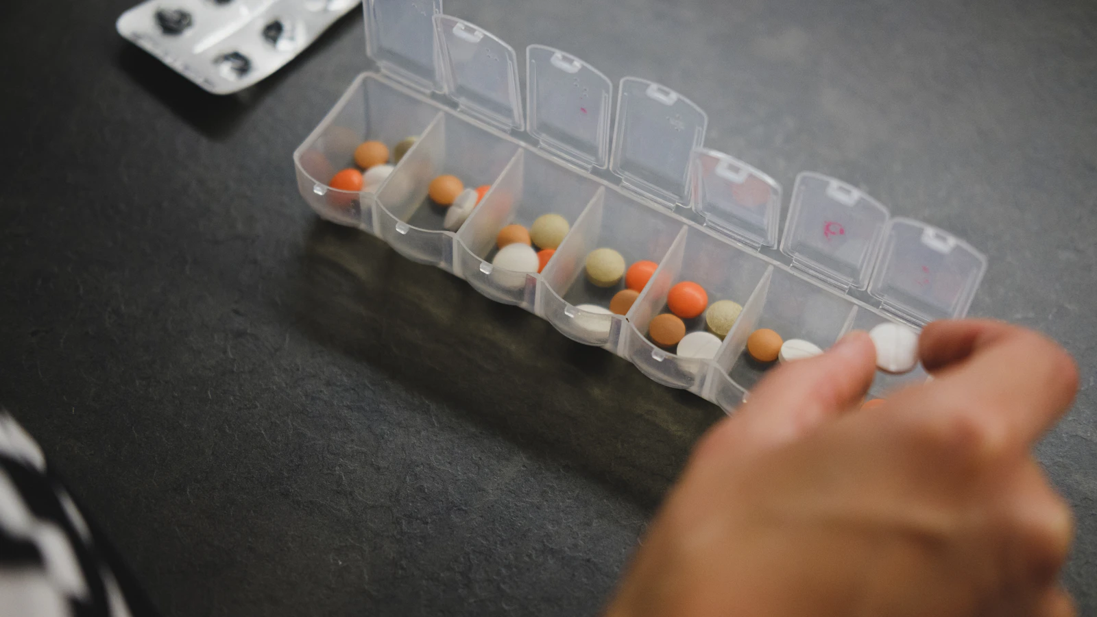 Een hand pakt een tablet uit een weekdoos met dagvakjes.