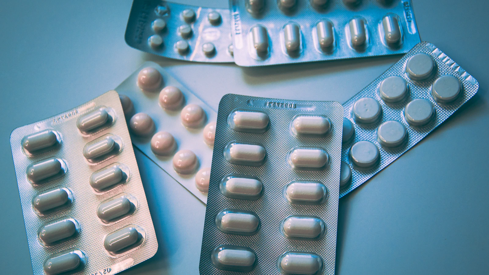 Doordrukstrips met witte en gekleurde tabletten op een blauwe ondergrond.