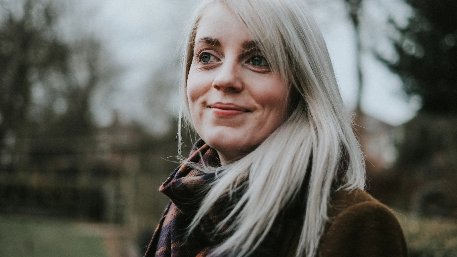 Vrouw met lichtblond haar kijkt ontspannen opzij in het buitenlicht.