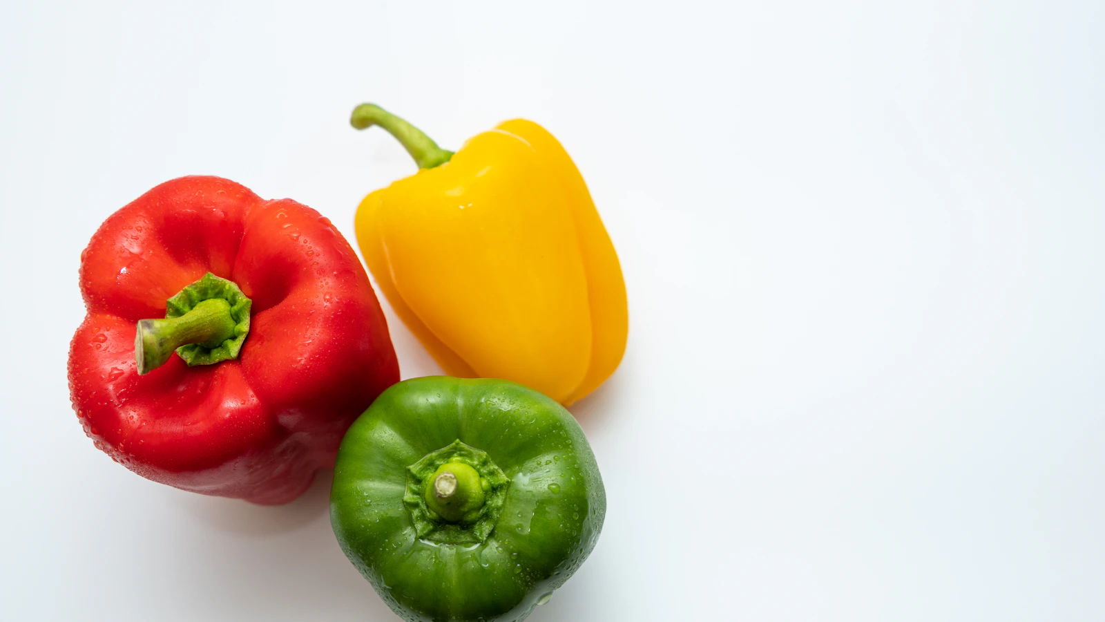 Een rode, gele en groene paprika op een witte ondergrond.