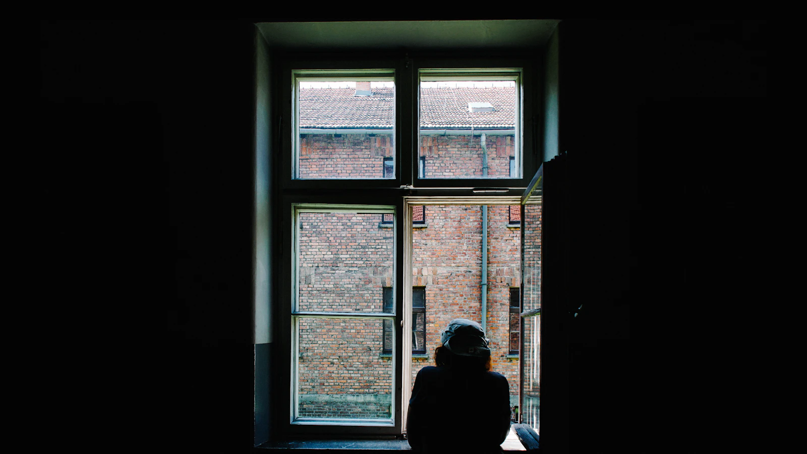 Persoon bij een open raam in het ochtendlicht, zonlicht helpt bij de aanmaak van vitamine D.