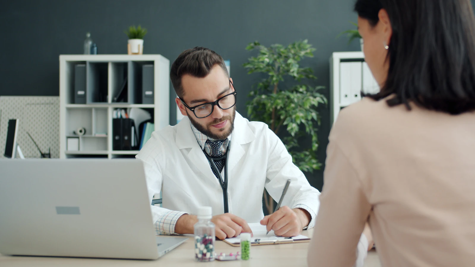 A doctor takes notes while a patient sits across from her.
